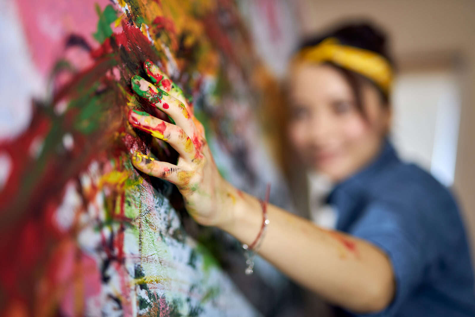 An artist's paint-covered hand working on a canvas